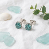 Blue moissanite studs flat-lay with sea glass and linen